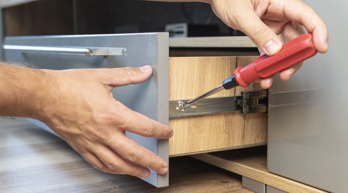 The man adjusts the drawer. Self-assembly of furniture. Young Handyman In Overall Installing Drawer In Kitchen - Maydek İnşaat İzmir